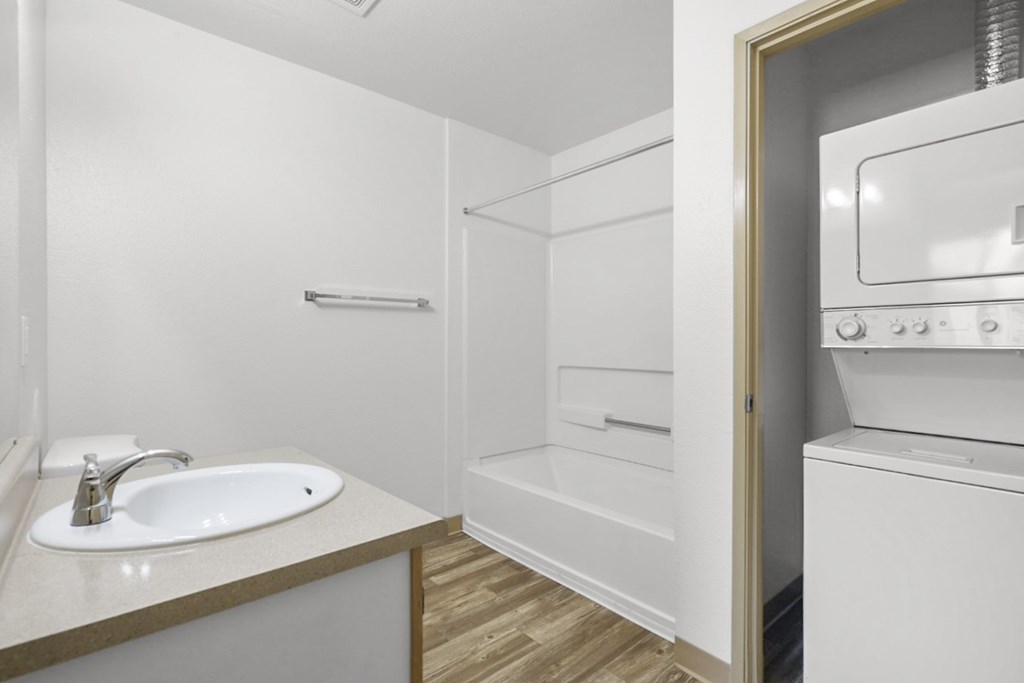 A white bathroom with a sink, mirror, and a washer and dryer.