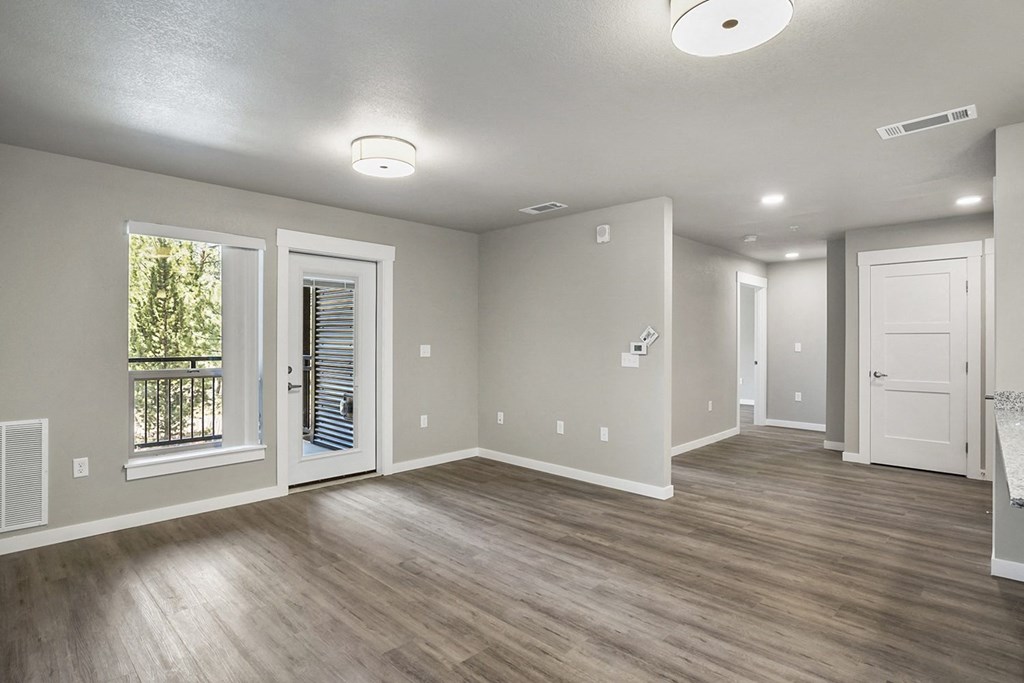 an empty living room with a kitchen in the background