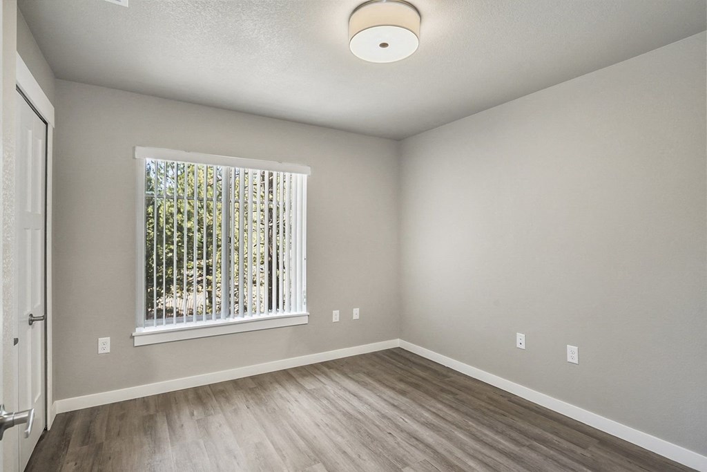 an empty bedroom with a large window and hardwood floors
