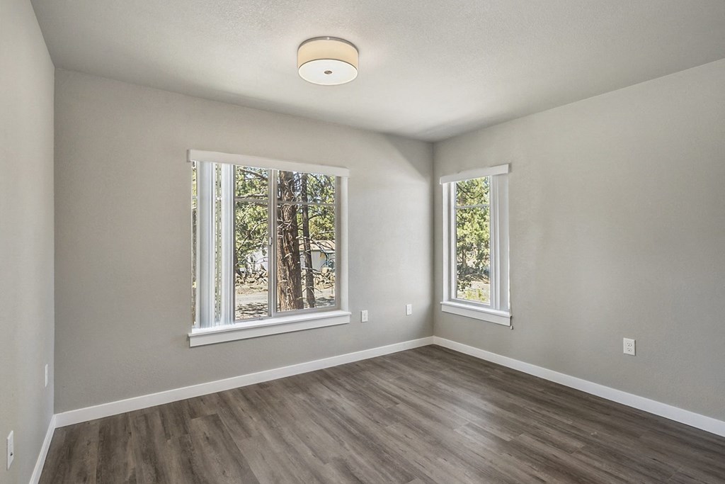 an empty bedroom with a large window and hardwood floors
