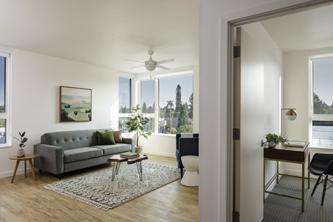 A living room with a grey couch and a painting on the wall.