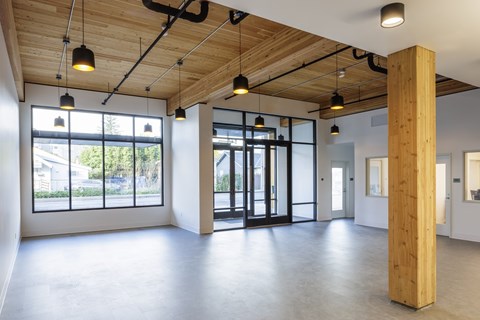 A spacious room with wooden beams on the ceiling and a large window on the left side.
