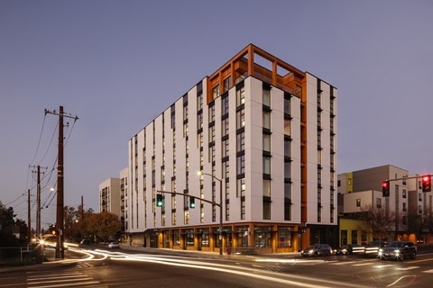 A modern building with a combination of white and wood panels is illuminated by street lights at dusk.