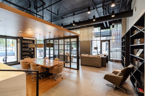 A modern office space with a long table and chairs, a bookshelf, and a window with a view of the street.