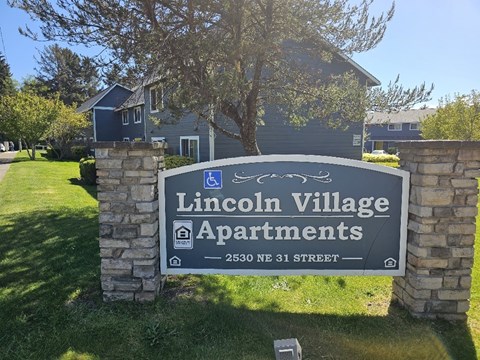 A sign for Lincoln Village Apartments stands in front of a building.