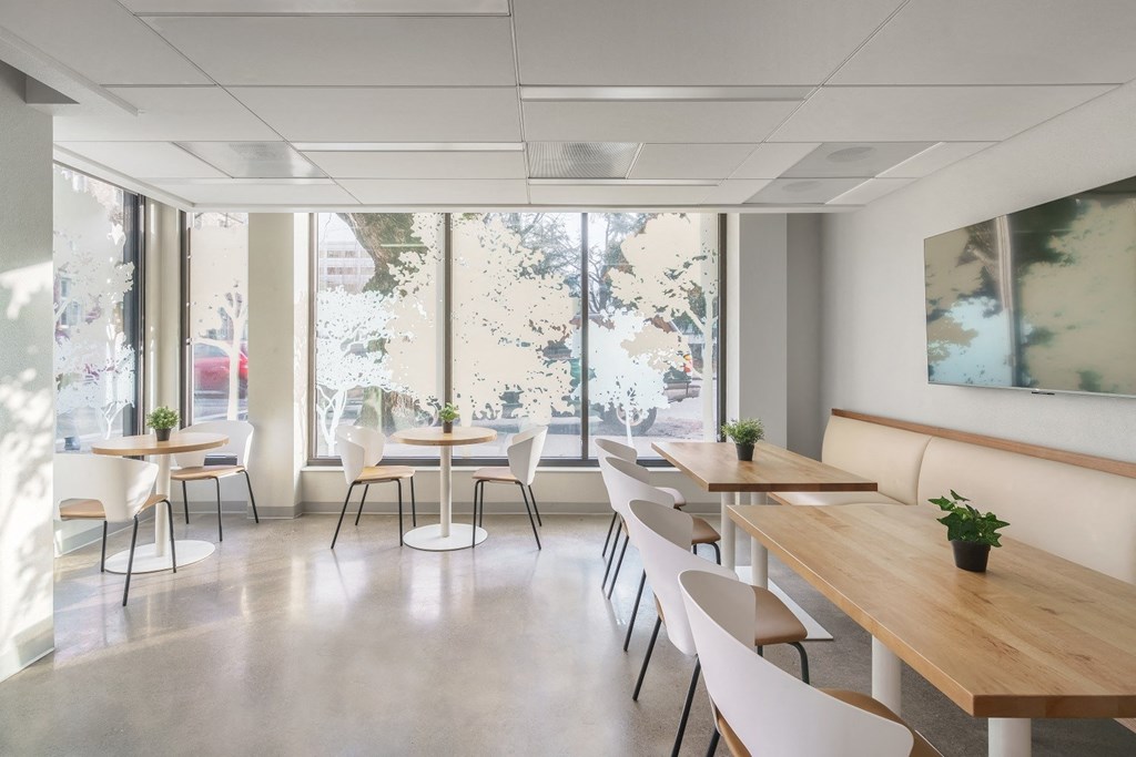 a room with wooden tables and white chairs with large windows in the background