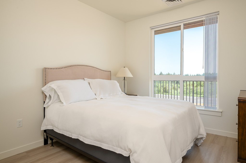 A bedroom with a large bed and a window overlooking a balcony.