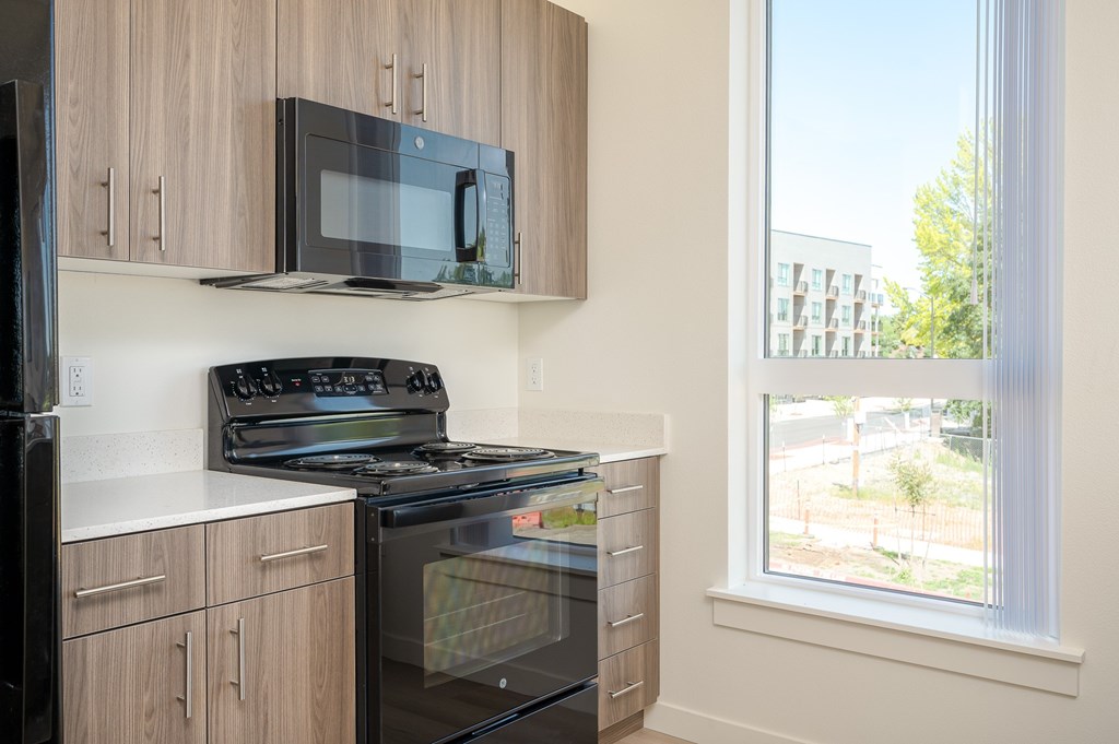 A black microwave is mounted on a wooden cabinet above a black stove.