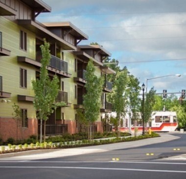 A train is coming down the tracks in front of a building.