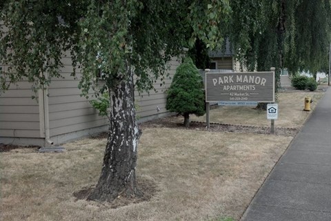 A sign for Park Manor Apartments is on a post in front of a tree.