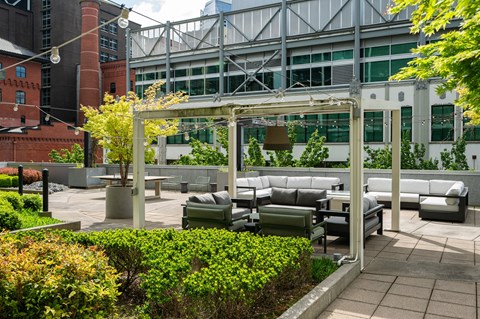 A patio with a white pergola and grey couches.