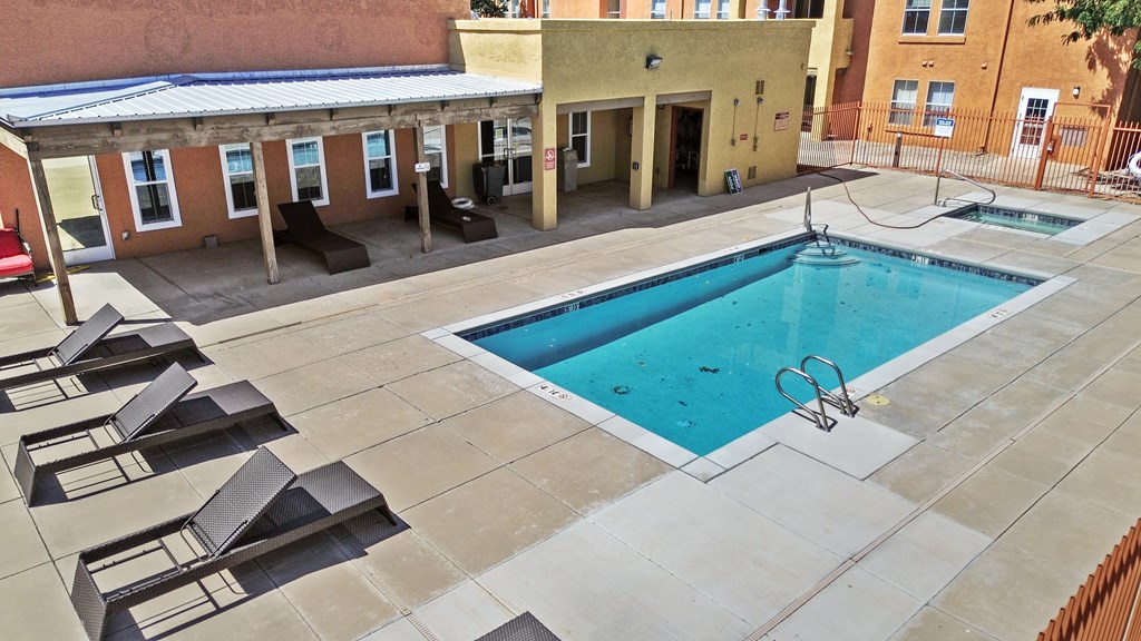 A swimming pool surrounded by sun loungers in a courtyard.