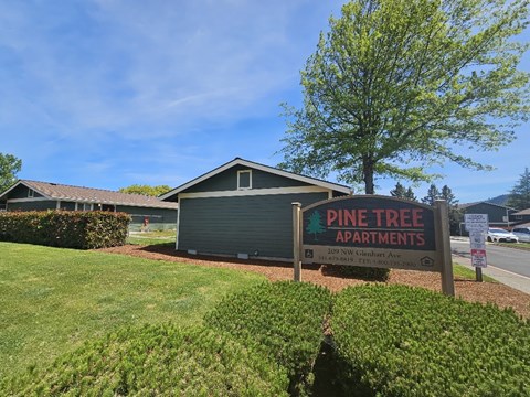 A sign for Pine Tree Apartments is in front of a green lawn.