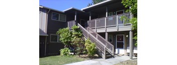 A brown house with a deck and stairs leading to the front door.