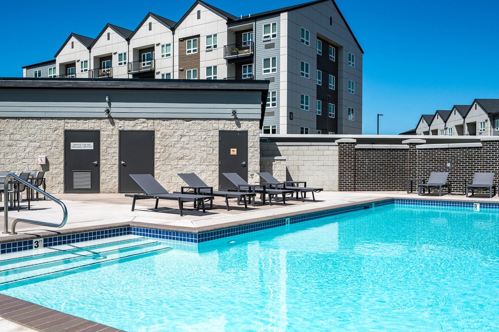a swimming pool with chairs and a building in the background