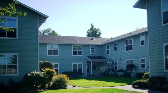 Apartment complex with green lawn and trees in the background.
