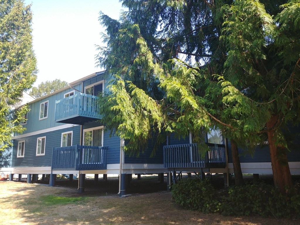 A blue house with a deck and trees in front.