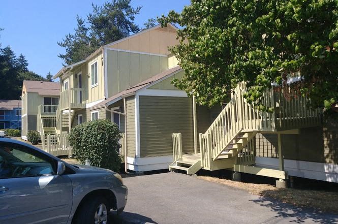 A silver car is parked in front of a two-story house with a garage and a staircase leading to the front door.