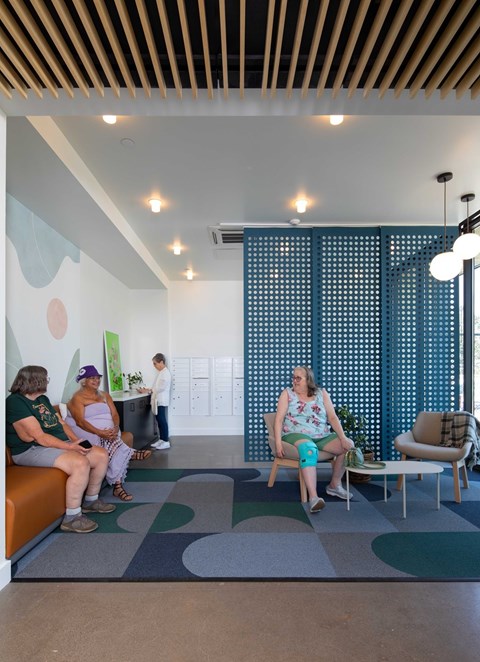 Three people sitting on a couch in a room with a blue screen behind them.