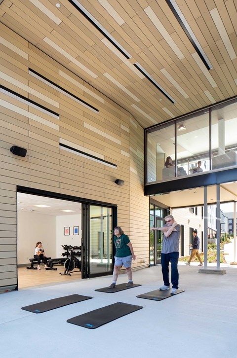 A man and a woman are exercising in a gym with wooden walls and ceiling.