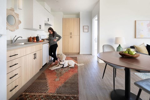 a woman standing in a kitchen with a dog on a rug