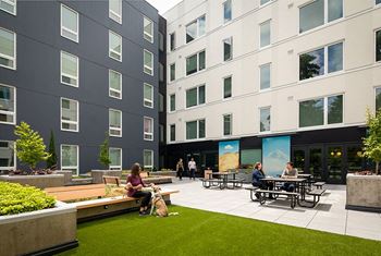 A man and woman are sitting at a picnic table in a courtyard between two buildings.