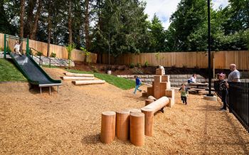 A playground with a green slide and brown sandbox.