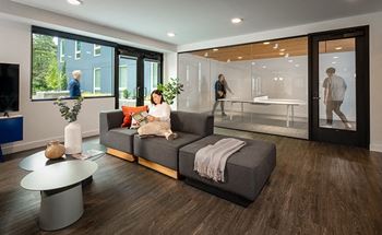 A woman is sitting on a grey couch in a modern living room.