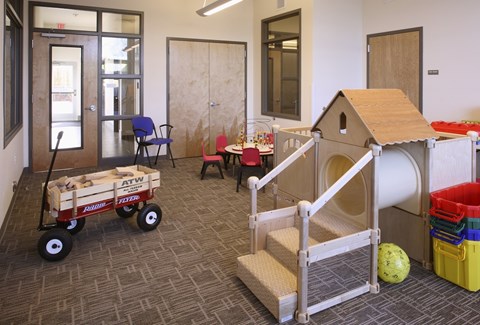 A child's play area with a wooden dollhouse, a wagon, and a ball.