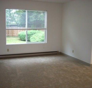 A room with a large window and a view of a green lawn and a wooden fence.
