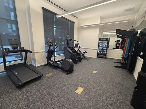 A gym with treadmills, elliptical machines, and a weight rack.