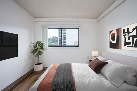 A bedroom with a bed, a potted plant, and a painting on the wall.