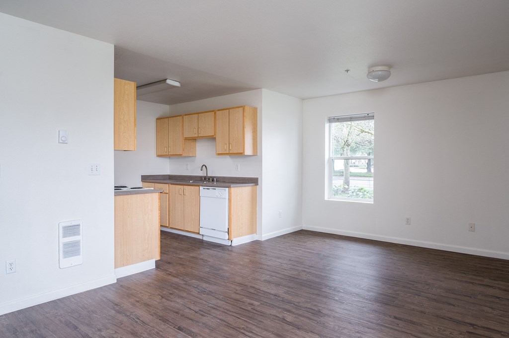 an empty living room with a kitchen in the background