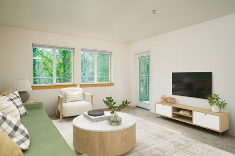 A living room with a green couch, a white chair, a round table, and a television.