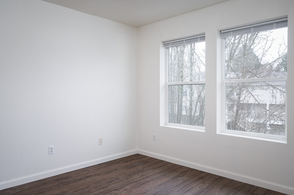 a bedroom with two large windows and a hardwood floor
