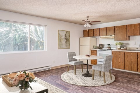 a living room with a table and a kitchen with a ceiling fan