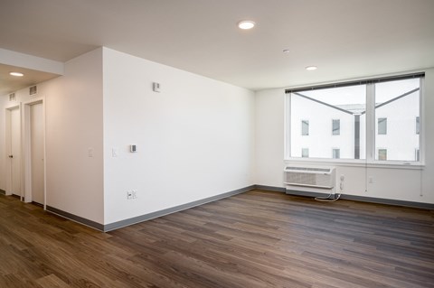 a living room with white walls and wood flooring and a large window