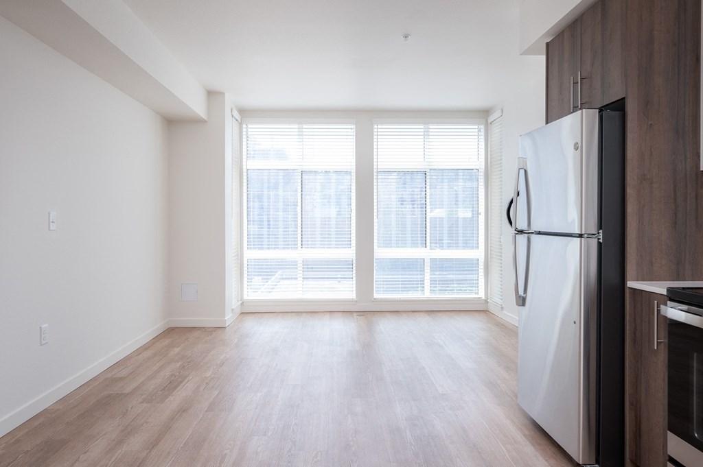 an empty living room with a large window and a refrigerator
