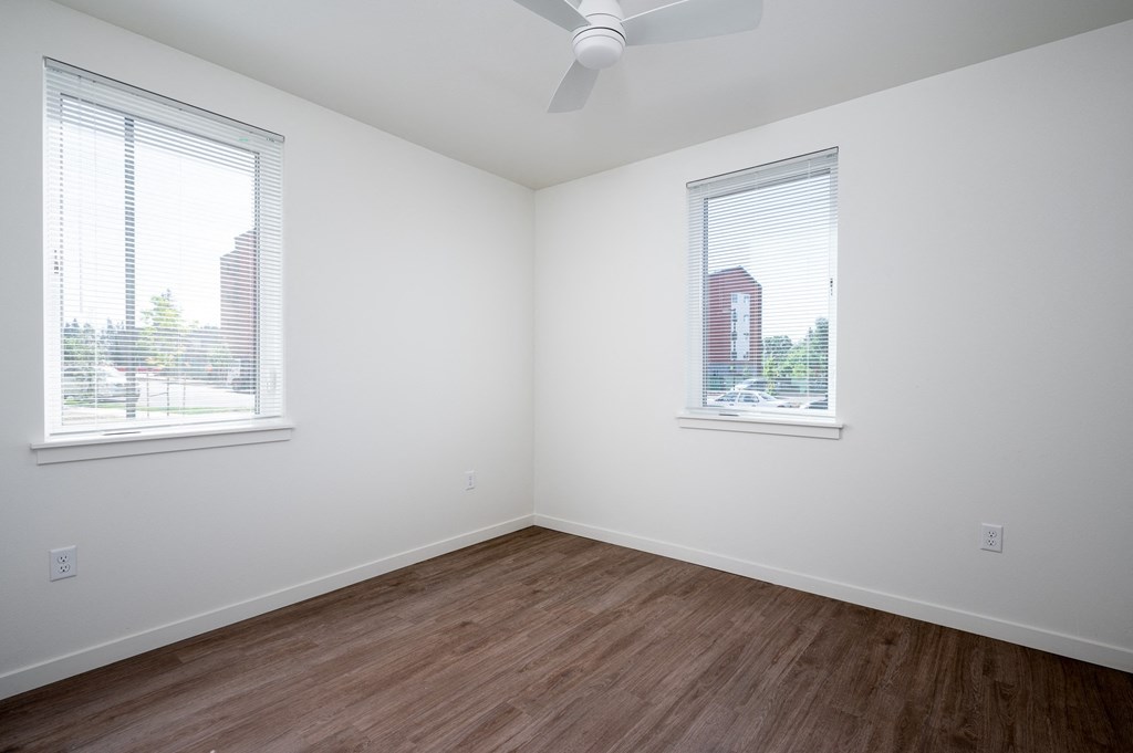 an empty room with wood floors and two windows