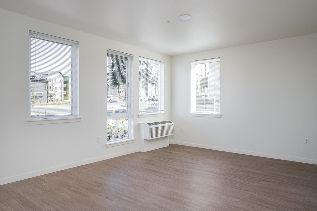 an empty living room with a wood floor and three windows