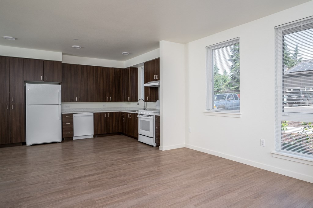 an empty kitchen with white appliances and wood flooring