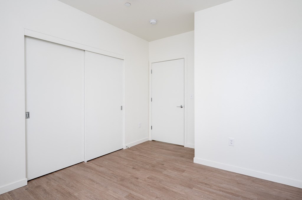 a bedroom with white walls and wood flooring and two closets