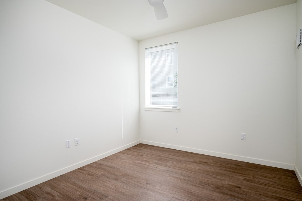 a bedroom with white walls and a window and wood floors