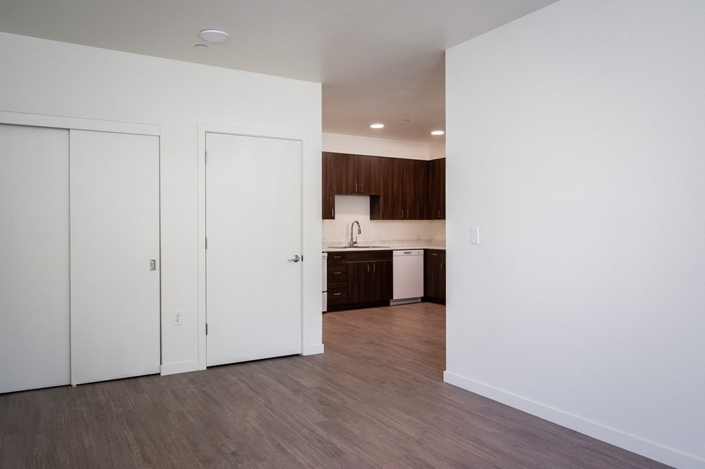 an empty living room and kitchen with white walls and wood flooring