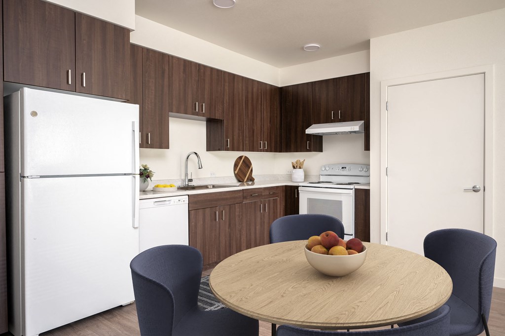a kitchen with white appliances and a table with a bowl of fruit