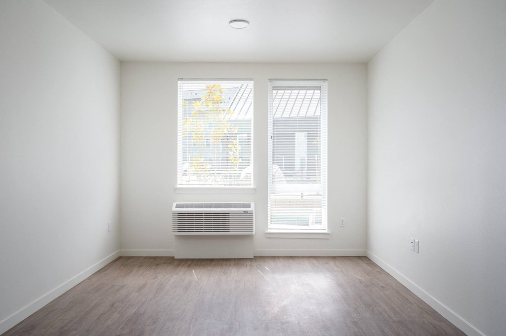 an empty room with two windows and wood floors