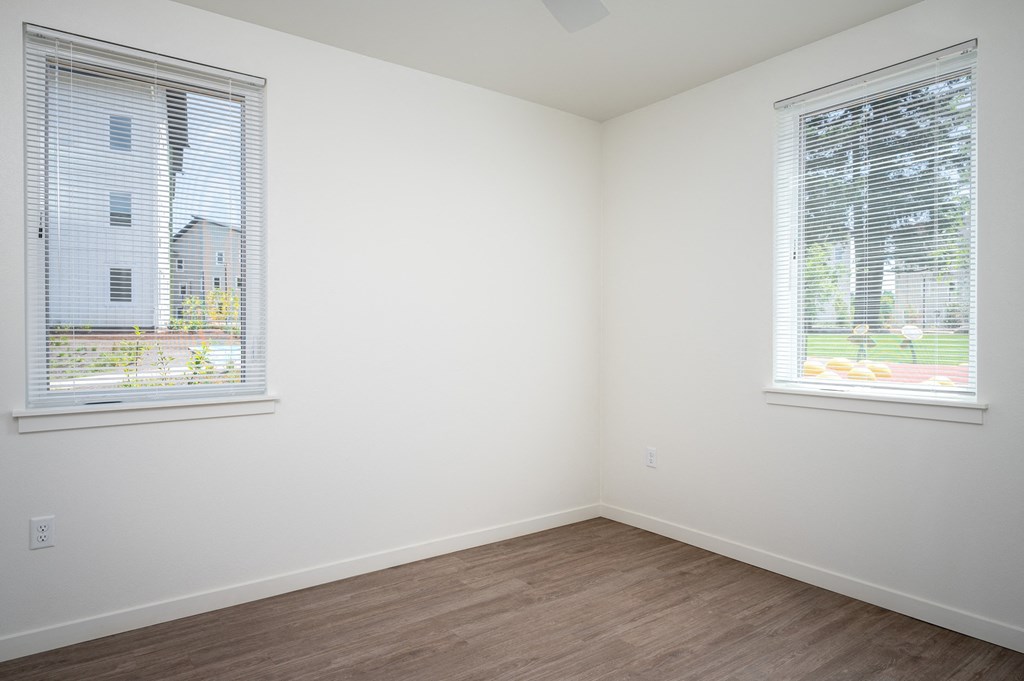 an empty room with two windows and a wooden floor