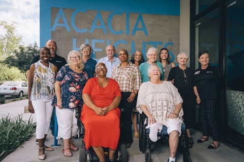 A group of people are standing in front of a blue building with the word "ACACIA" on it.