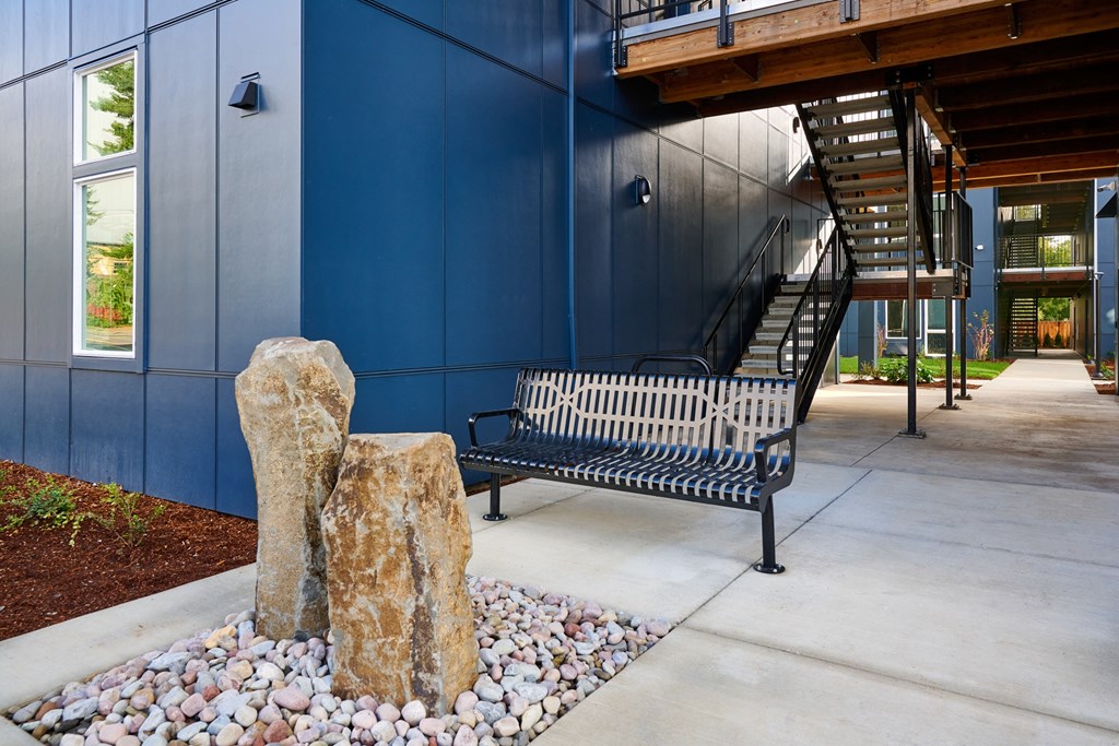 a bench and rocks in front of a blue building with a staircase