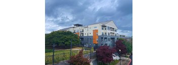 A modern building with a mix of grey and orange accents sits in a residential area.